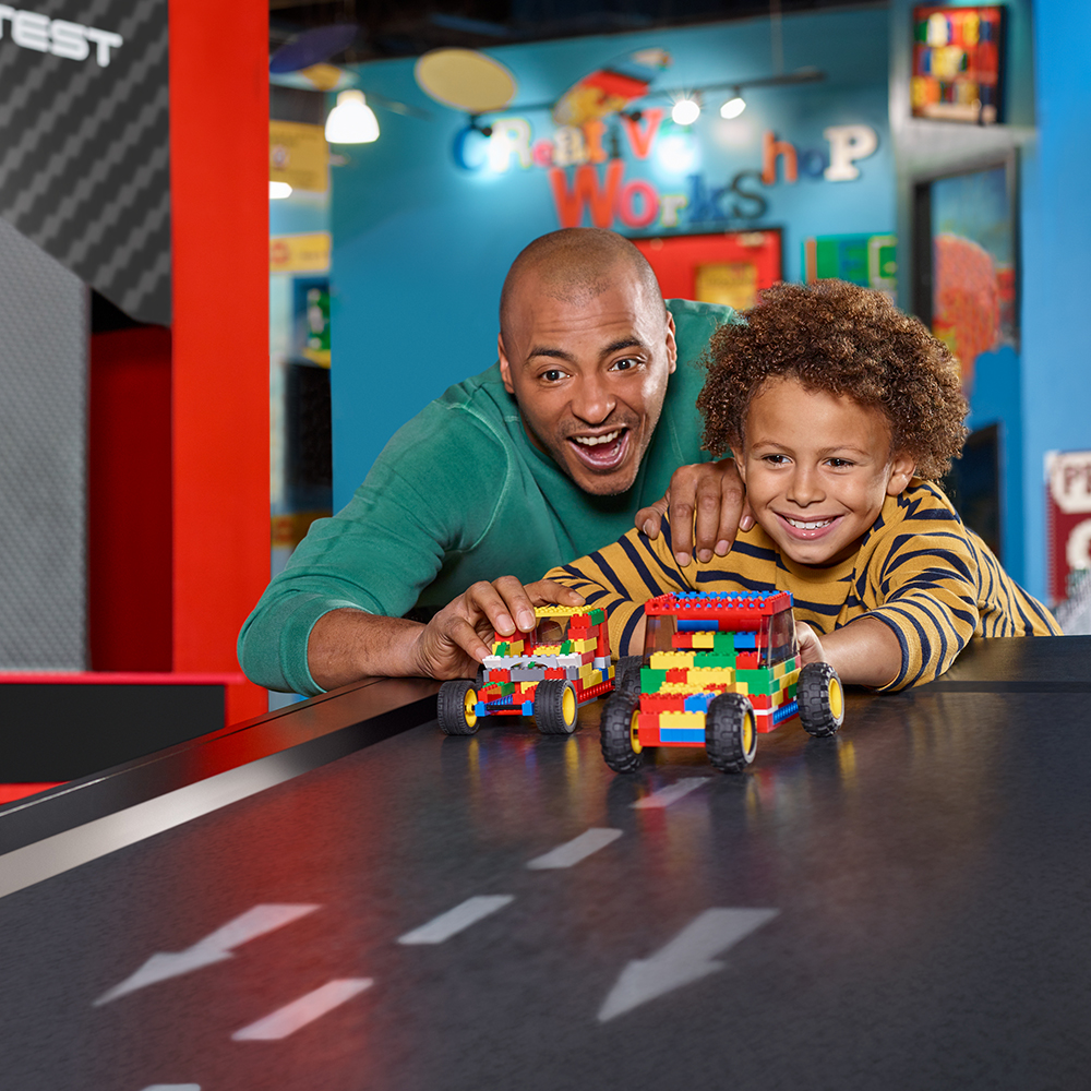 Dad and son racing LEGO cars down a ramp at LEGOLAND Discovery Center Bay Area