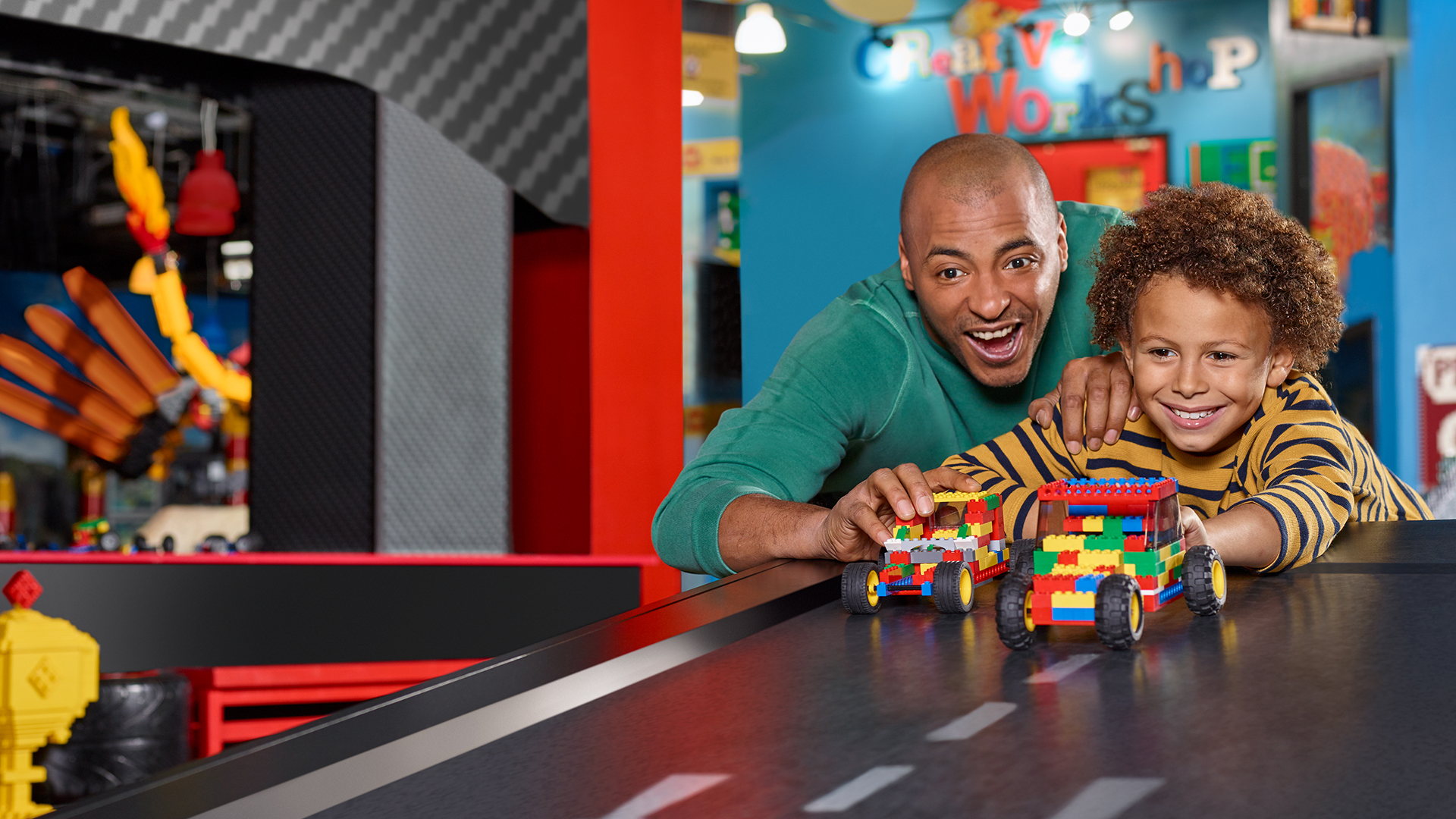 An excited adult and child racing colorful LEGO cars at the LEGOLAND Discovery Center's creative workshop.